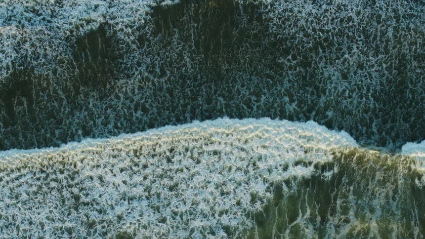 Aerial view of ocean waves breaking against the beach