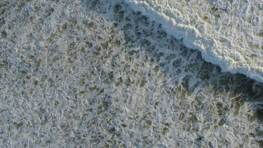 Aerial view of white ocean waves breaking against the shore