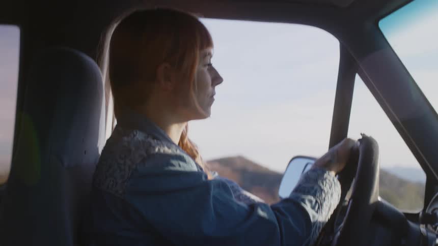 A woman is driving an automobile with mountains in the distance