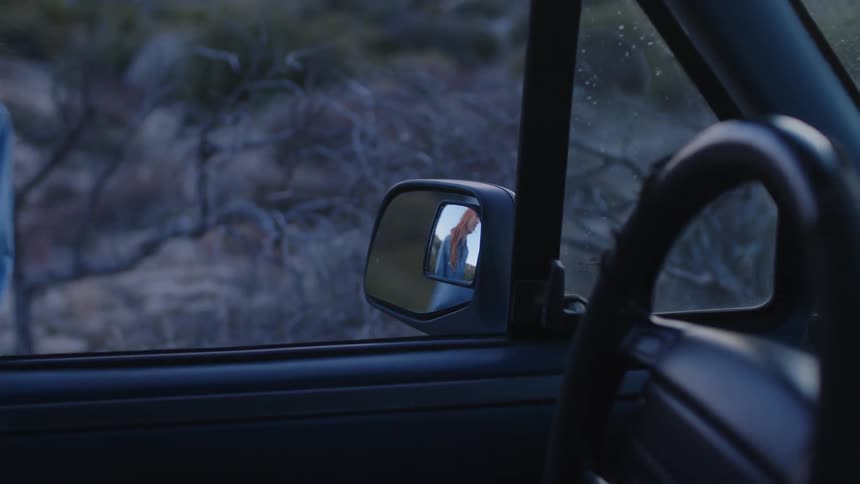 A woman with red hair and a blue shirt gets into a white pickup truck in the terrain