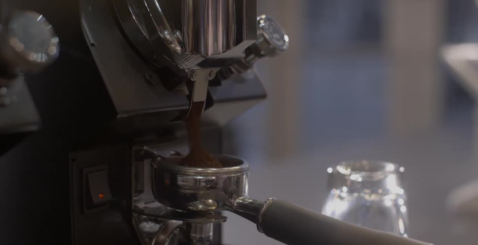 A barista adjusts a coffee machine pouring coffee grounds