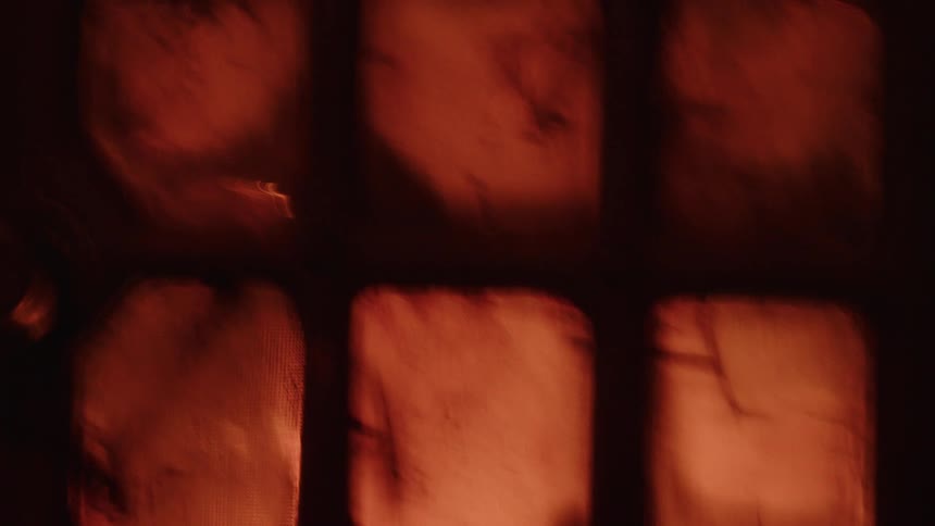 Flashing lights shine through a gridded window with orange tint