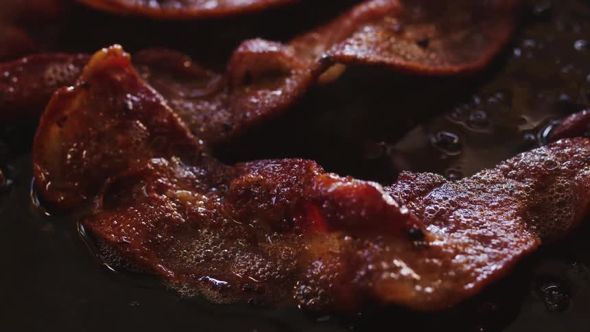 Close up of bacon frying on a pan