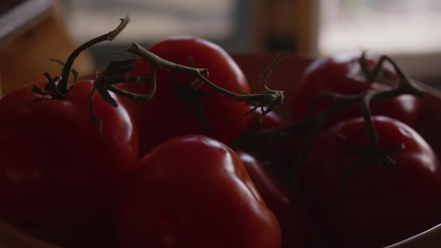 An adult picks a fresh tomato from bowl of tomatoes