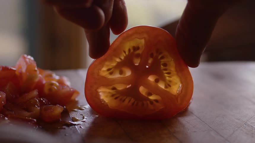 A person cutting a tomato slice using a large knife