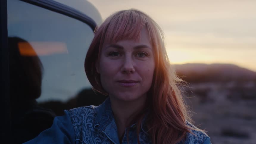 Woman reclined on a car parked in the desert at sunset