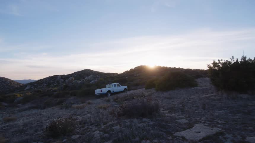 White pickup truck drives down the terrain at sunset traversing the landscape with a golden glow