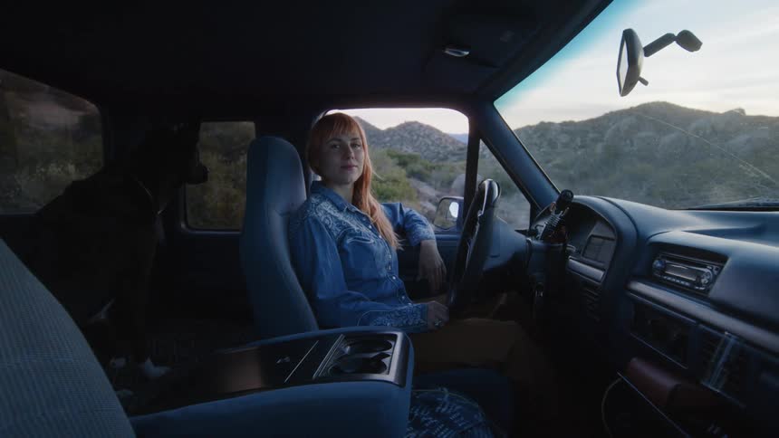 Lady sits inside a parked car at daytime with a dog at the back sit