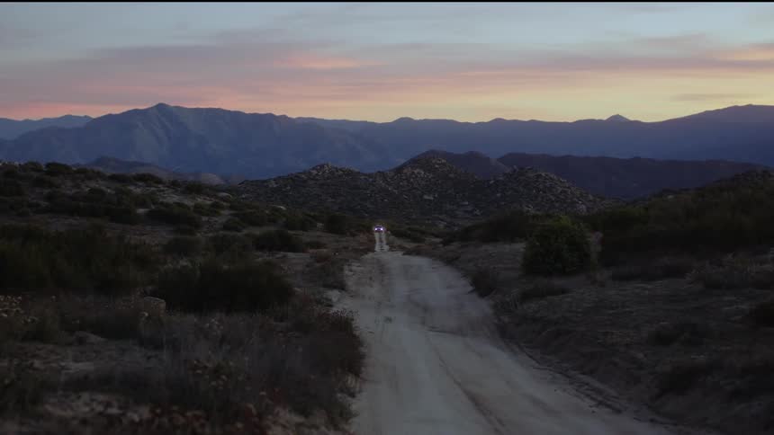 Pickup truck driving down dirt road in the field at dusk