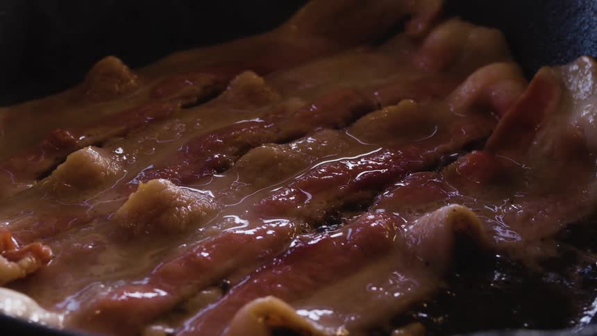 Slices of bacon cook in a frying pan