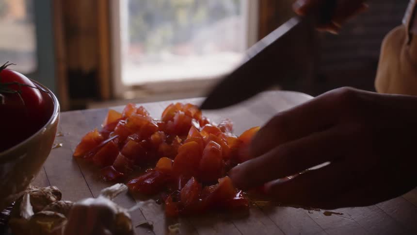 Man cuts up tomatoes on wooden table in the kitchen