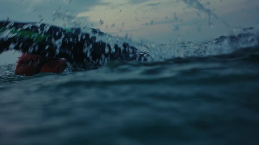 Person wearing wet suit and a cap swims through ocean