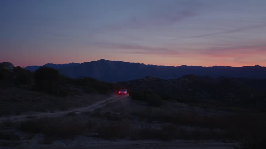 White pickup truck drives along dirt track in the field at sunset