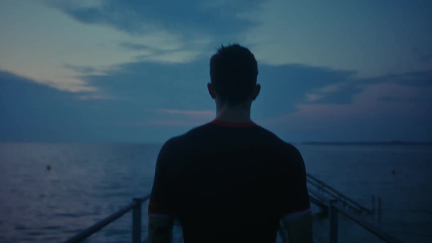 A man shown from behind is walking down a pier at the ocean