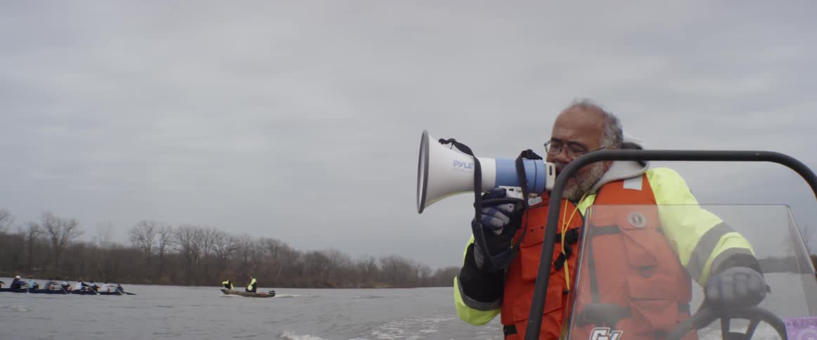 Man in orange life jacket driving a boat speaks through a megaphone