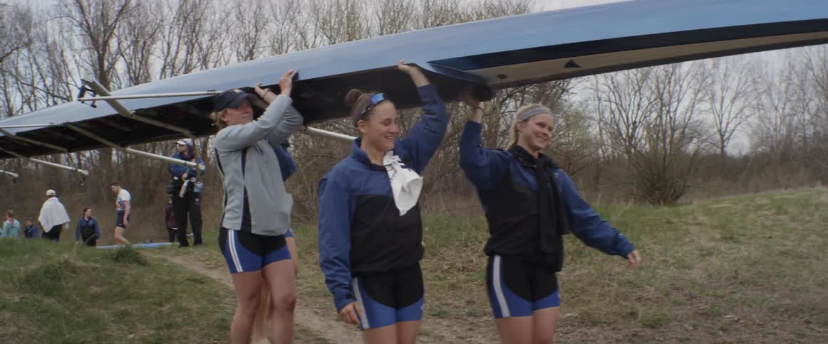 People carry a long canoe downhill on a cloudy day