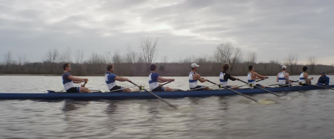 Male rowers row in unison on an overcast day