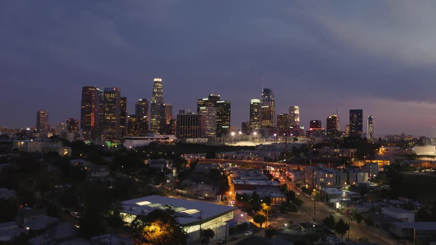 Cars travel down a lit city road with a city skyline in the background