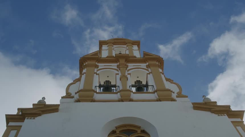 Upward view of the facade of a white church with two bells on a day with a blue sky and clouds