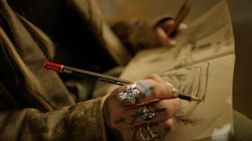 Tattooed artist wearing large rings drawing on paper