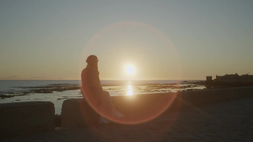 Silhouette of a person sitting next to the coast at sunset