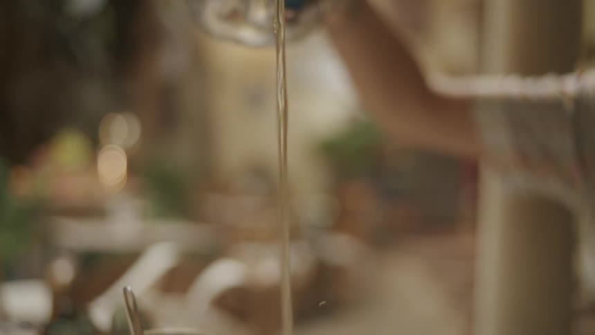 Closeup of a womans hands pouring tea from a teapot into a glass