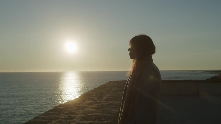 A woman is watching the sunrise by the shore