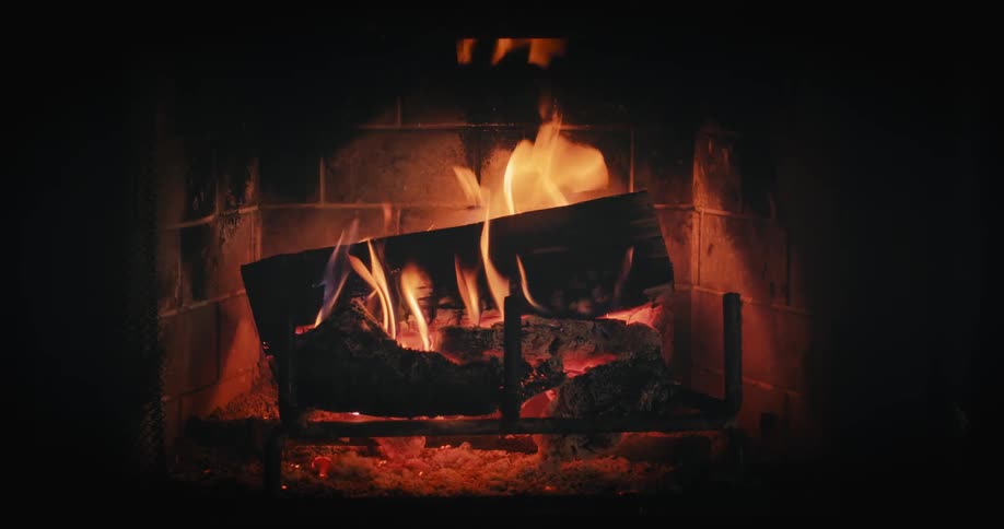 Flames flicker and waver and sparks fly as wood burns and falls in a fireplace