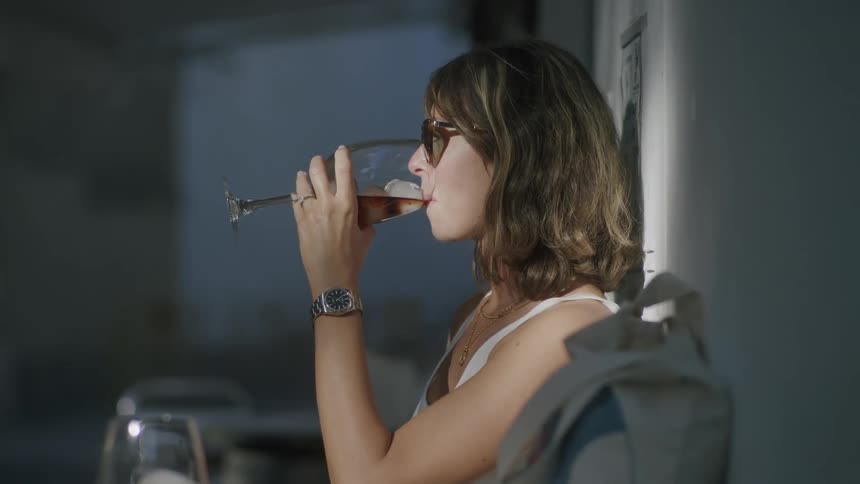 Woman sitting sipping a drink from a glass with ice