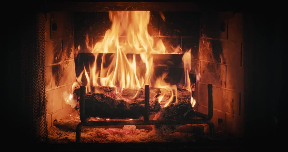 Flames of logs burning in a fireplace wave wildly in the darkness