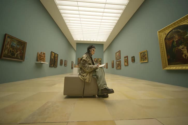 A woman is sitting in an art gallery and is drawing