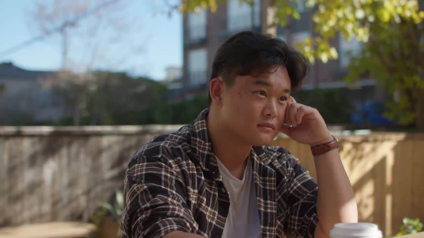Young man sitting in the backyard laughs listening to a friend