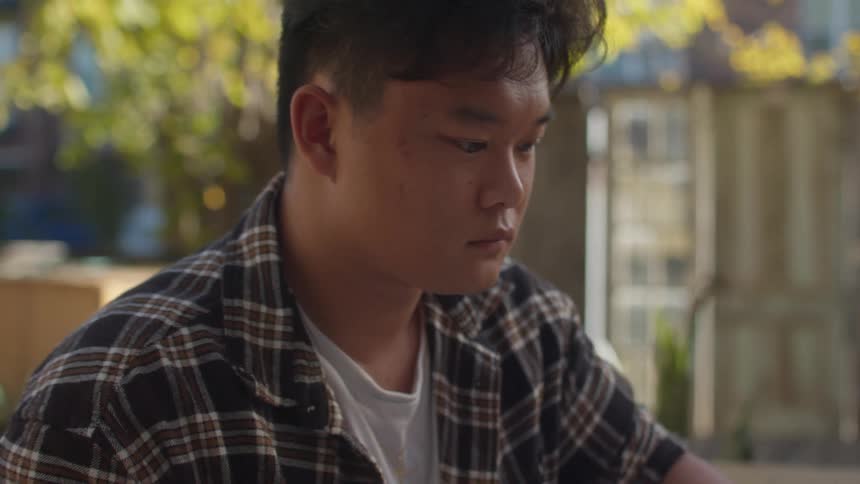 Man with a plaid shirt sits at table studying in cafe yard