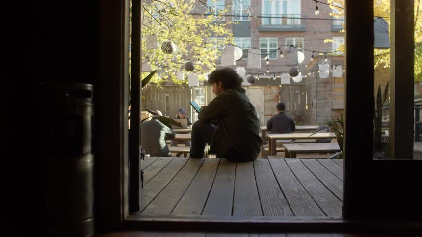 Man sits on porch across from apartment building and scrolls on smartphone