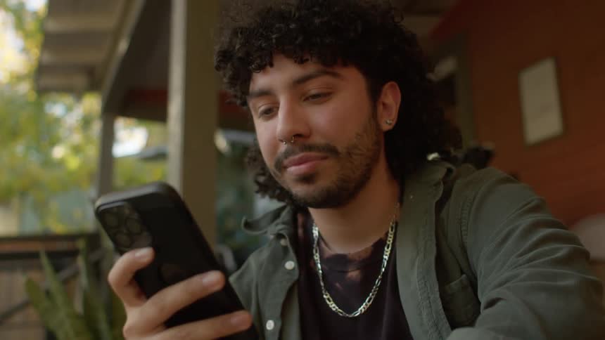 A man sitting on his front porch nods his head as he looks at his phone