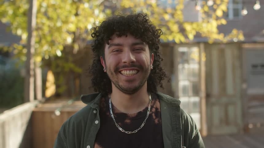 A man is standing outside with a fence in the background and he smiles