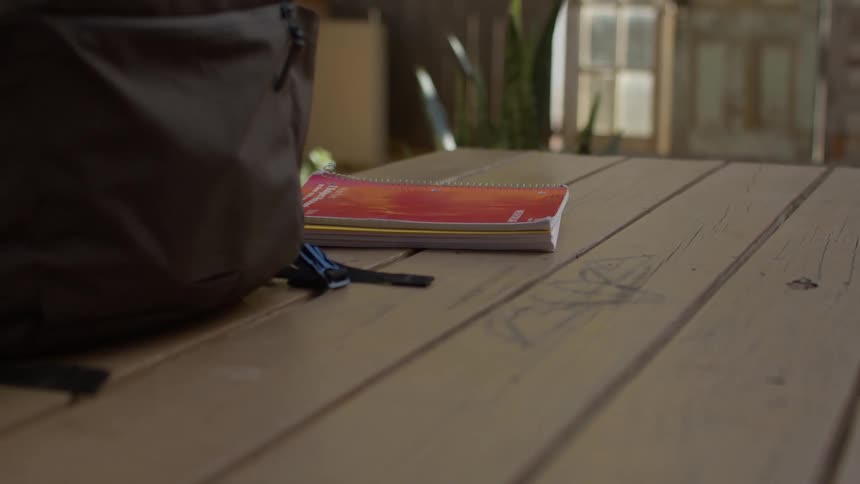 A human hand picking up some notebooks that are on a table next to a backpack