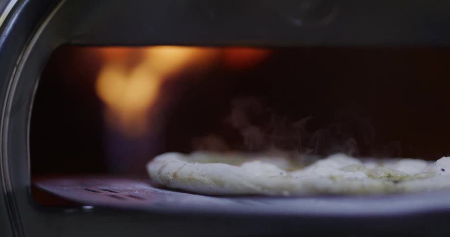 Person uses a peel to pull a hot pizza out of a burning pizza oven