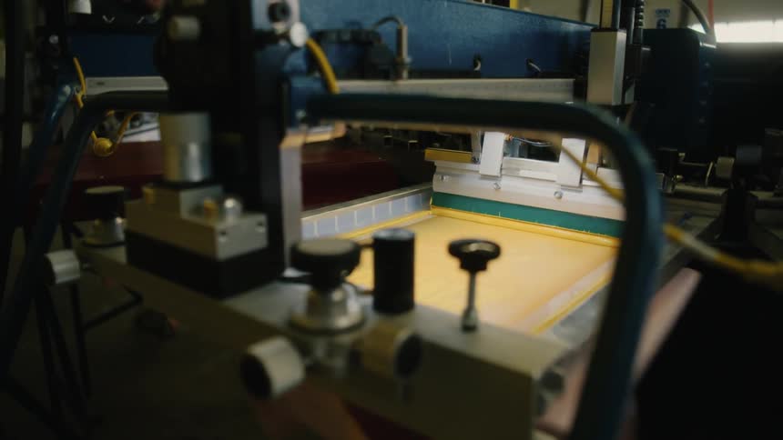 Shirt pulls under tray of yellow ink on a machine in a screen print factory