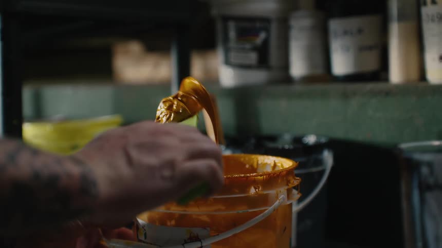 Artist picks up yellow paint from a bucket