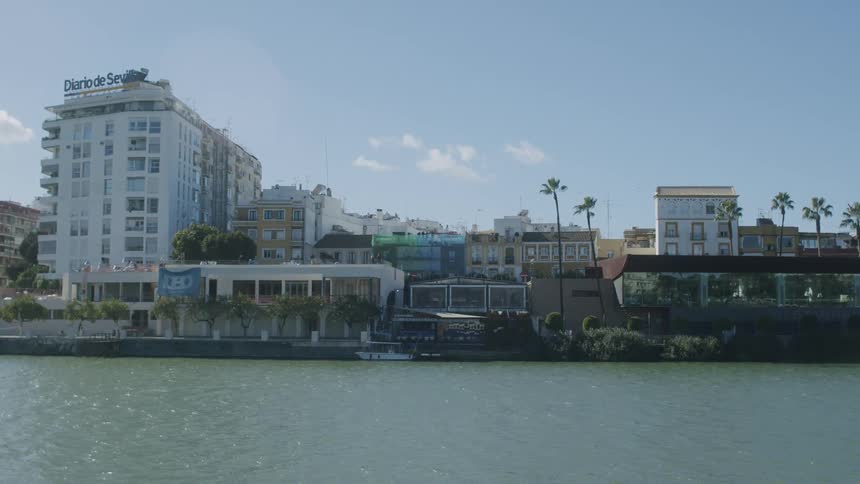 Waterfront properties with a large white hotel building and palm trees on a bright day