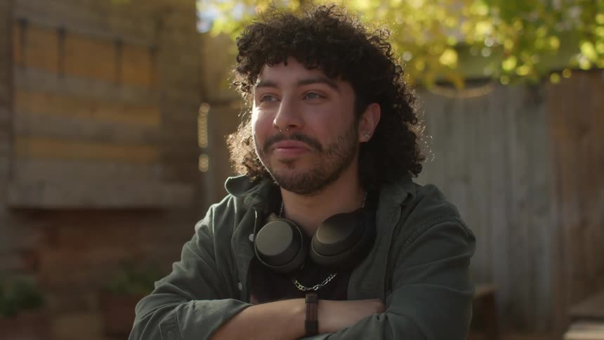 A man with headphones around his neck is sitting outside smiling and nodding his head in agreement