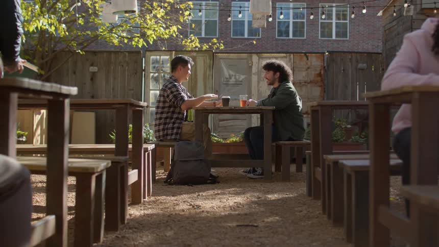 Two teenagers sitting at a table sipping drinks from cups and engaged in conversation with each other