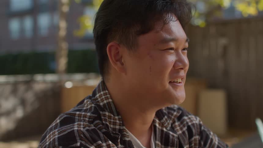 A face of a young asian boy wearing a plaid shirt is talking and starts laughing