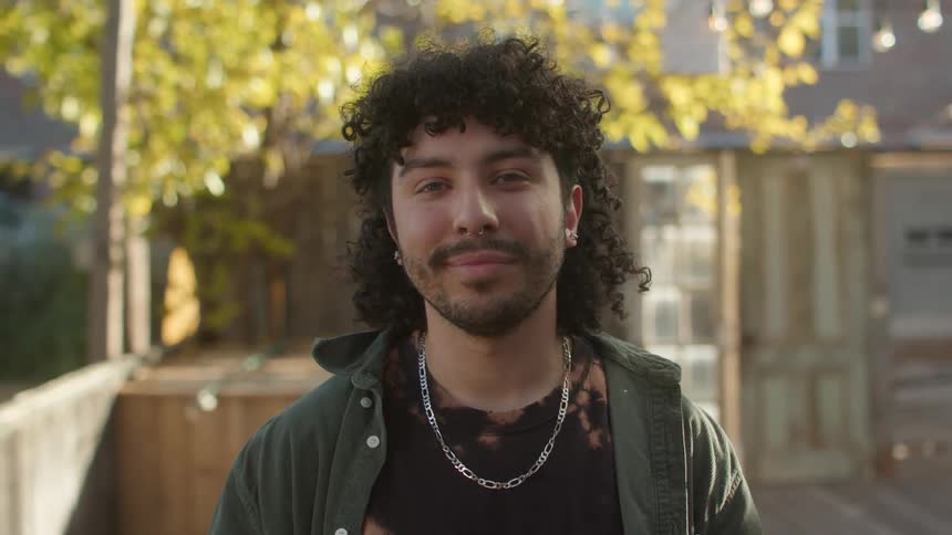 A man is standing outside as he turns his head and smiles