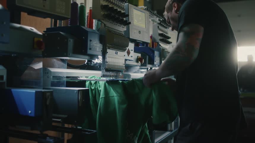 Man places and adjusts shirt on industrial sewing machine in shop