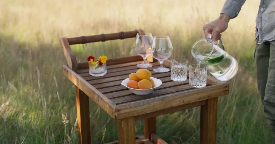 A man comes to a small wooden table and pours water into an empty glass