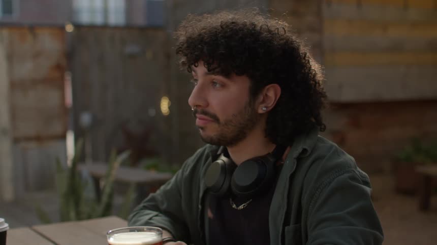 A young man sit outdoors while drinking beer and talking with a friend