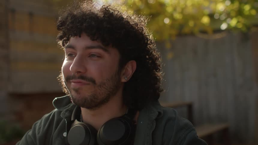 A bearded man with curly hair and headphones giving an approving nod in the yard