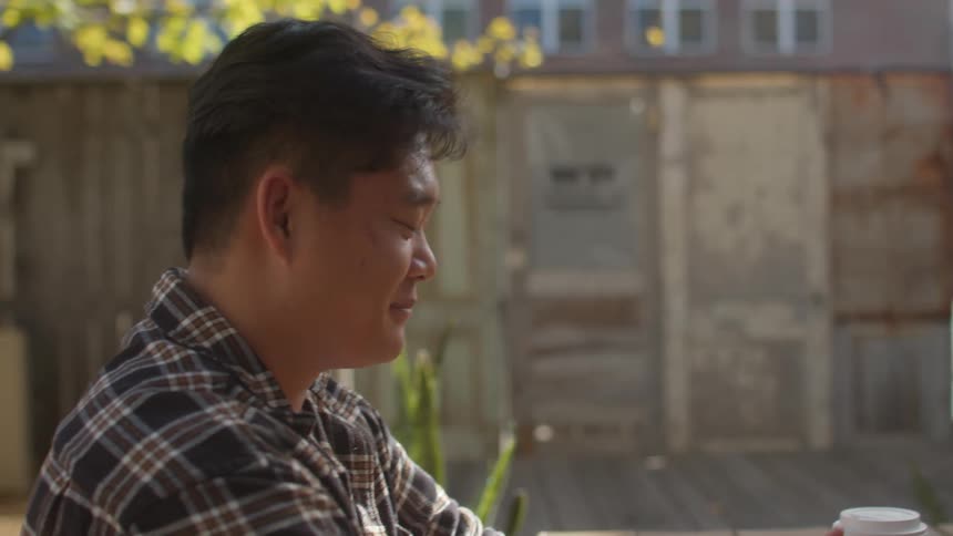Two friends sitting at a table in the backyard with drinks on the table having a conversation